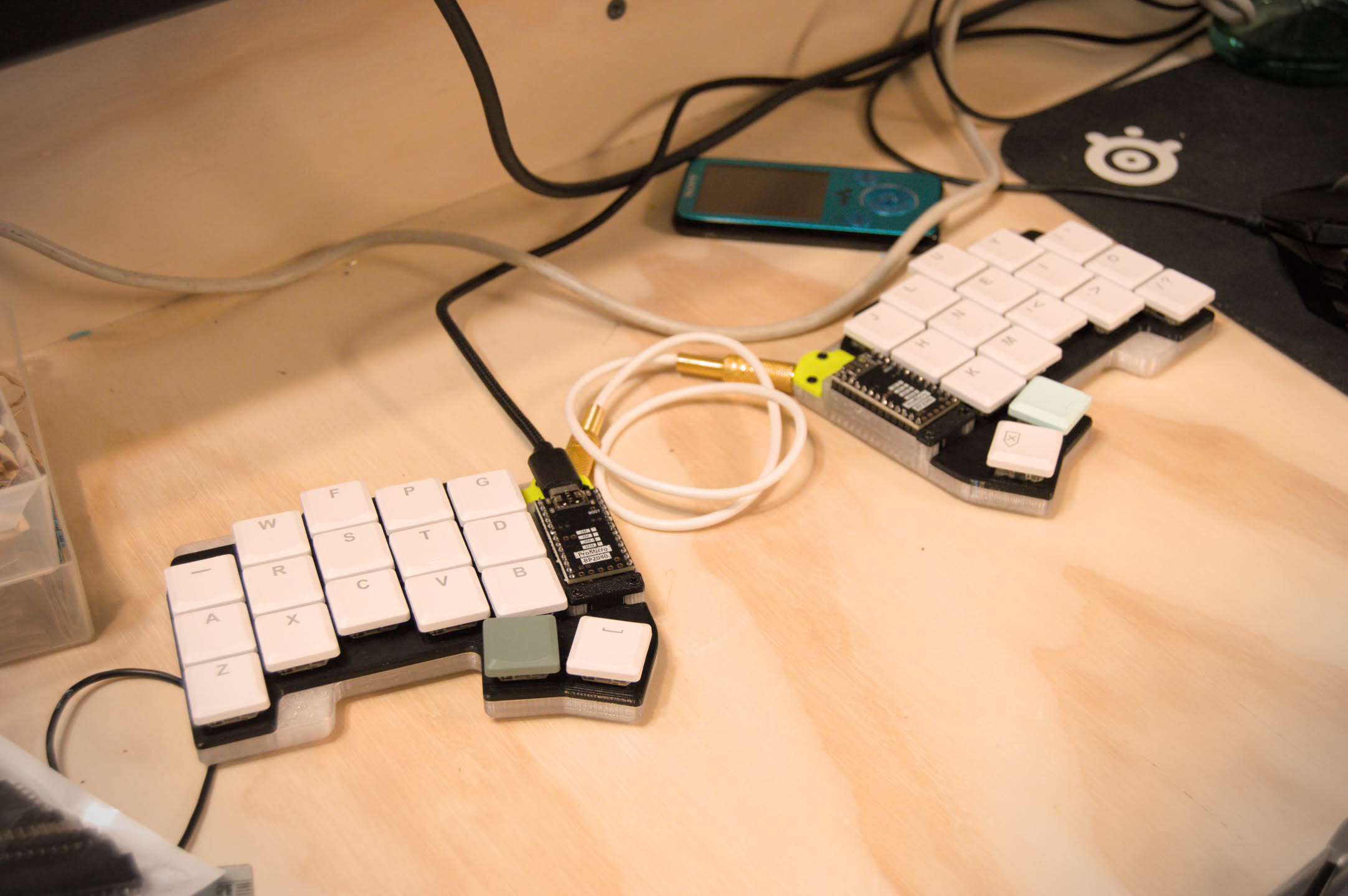 a photo of the ferric keyboard on a wooden computer desk, surrounded with other small electronics.